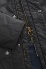 Close-up front view of the Barbour Wax parka 'Bedale' navy showing waxed cotton fabric, brass two-way zip with ring pull, snap buttons, and signature tartan lining.