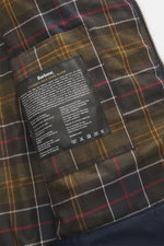 Close-up inside view of the Barbour Wax parka 'Bedale' navy showing the signature tartan lining and Classic Wax Care Guide label. An icon among wax jackets, the BARBOUR 'Bedale' returns this season as a parka, with extra length and even more protection. H