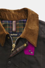 Barbour Wachsjacke 'Gamefair' dunkelgrün, Nahaufnahme von Cordkragen, Tartan-Innenfutter, Reißverschluss und Druckknöpfen, von oben fotografiert.