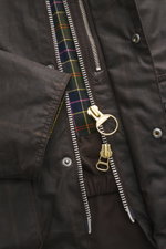Nahaufnahme der Barbour Wachsjacke 'Gamefair' dunkelgrün, seitlich fotografiert, zeigt gewachste Baumwolle, goldenen Zwei-Wege-Reißverschluss und Tartan-Innenfutter.