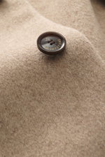 Nahaufnahme eines braunen MONTECORE-Knopfs auf der weichen, melierten Oberfläche der Montecore Cashmere Jacke beige meliert aus reinem Cashmere.