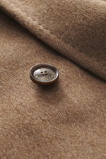 Close-up of the Montecore Cashmere Jacket taupe melange fabric and branded button, showing texture and detail from a front angle. Luxurious through autumn and winter: MONTECORE presents this model made of pure cashmere as an elegant companion for the cold