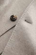 Nahaufnahme der beige melierten Brunello Cucinelli Cashmere Jacke mit Knopf und Knopfloch, weiche, wasserabweisende Cashmere-Qualität sichtbar.