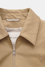 Nahaufnahme von Kragen und Reißverschluss des Ami Paris Blouson beige, Twill Baumwolle, Regular Fit, Unisex, mit logo-Stitching, elastischen Abschlüssen.