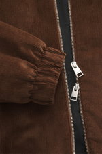 Nahaufnahme aus schräger Perspektive des braunen Ami Paris Cord-Blouson mit robustem Zwei-Wege-Reißverschluss, elastischem Saumabschluss und weichem Griff.
