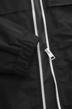 Schwarz fotografierter Ami Paris Blouson 'Windbreaker' im Close-up mit hochwertiger Microfaser, glattem Griff, Regular Fit, robustem Reißverschluss, versteckter Kapuze, paspelierten Fronttaschen mit Knopf, Logo-Detail, elastischen Saum- und Ärmelbündchen,