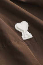 Nahaufnahme des weißen Logo-Details auf brauner Microfaser des Ami Paris Blouson 'Windbreaker' braun mit glattem Griff.