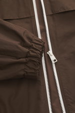 Nahaufnahme des braunen Ami Paris Blouson 'Windbreaker' aus hochwertiger Microfaser, glattem Griff, Regular Fit, robustem Reißverschluss, elastischem Ärmelbündchen, paspelierten Fronttaschen, versteckter Kapuze im Kragen, Logo-Detail auf der Brust und ges