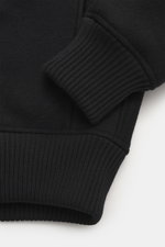 Close-up from above of the Jacquemus Blouson black showing pure new wool, soft touch, oversized fit, turn-down collar, smooth button placket, piped front pockets, elastic hem and sleeve cuffs.