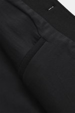 Close-up detail of Jacquemus Blouson black showing piped front pocket and button placket, photographed from above; pure new wool, soft touch, oversized fit, turn-down collar, smooth button placket, piped front pockets, elastic hem and sleeve cuffs.