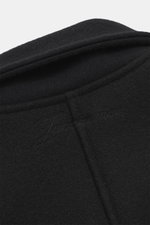 Close-up top-down view of Jacquemus Blouson black showing pure new wool fabric with soft touch, turn-down collar, smooth button placket, piped front pockets, elastic hem and sleeve cuffs, and oversized fit.