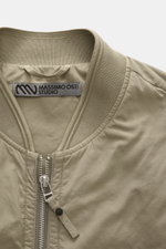 Nahaufnahme der Massimo Osti Studio Jacke taupe von oben, Slim Fit, hochwertige Microfaser, weicher Griff, matte Optik, PrimaLoft® Wattierung, garment dyed, robuster Reißverschluss, Blousonkragen, Seitentaschen mit Druckknöpfen, regulierbarer Saum, Metall