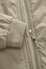 Nahaufnahme der Massimo Osti Studio Jacke taupe von vorne mit Fokus auf robusten Reißverschluss, geripptes Ärmelbündchen, hochwertige Microfaser mit weichem Griff, matter Optik und Slim Fit.