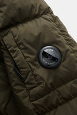 Nahaufnahme der rechten Ärmelpartie der C.P. Company Daunenjacke 'Nycra-R' dark olive mit hochwertiger, recycelter Microfaser, wasserabweisend, Slim Fit, Kapuze mit Tunnelzug und Zipper-Tasche mit Linsen-Detail, fotografiert von oben.