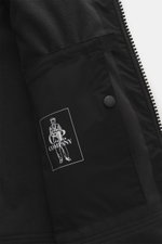 Close-up inside view of C.P. Company Parka 'Long Jacket' schwarz showing black fleece lining, inner pocket with logo, and zip detail.