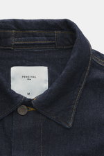 Nahaufnahme der Percival Jeansjacke 'Western Trucker' navy aus reinem Baumwoll-Denim, Fokus auf Umlegekragen und Logoetikett, von oben fotografiert.