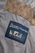 Nahe Aufnahme des Innenfutters vom Herno Daunen-Steppmantel grau, mit Label und gebrandetem Webpelzkragen.