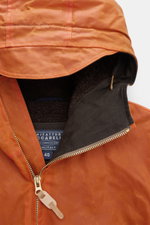 Close-up front view of the hood and collar of the Manifattura Ceccarelli Waxed jacket 'Blazer Coat' orange, showing waxed cotton fabric, super-soft wool lining, leather zipper pull, and adjustable hood with peak. The waxed jacket 'Blazer Coat' by MANIFATT