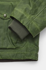 Manifattura Ceccarelli Wachsjacke 'Blazer Coat' grün, Detailaufnahme von Ärmelsaum und Fronttasche aus gewachster Baumwolle mit Lederdetails, wasserabweisend.