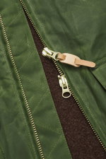 Nahaufnahme der Manifattura Ceccarelli Wachsjacke 'Blazer Coat' grün, Fokus auf wasserabweisenden Baumwollstoff, Lederdetails und robusten Zwei-Wege-Reißverschluss.