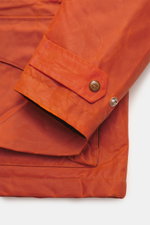 Close-up front-side view of the sleeve and lower pocket of the Manifattura Ceccarelli Waxed jacket 'Weekender' orange, showing waxed cotton with typical material feel, water-repellent fabric, slim fit, light padding of pure wool, two-way zipper, wind flap