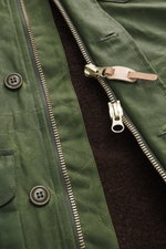 Nahaufnahme der Manifattura Ceccarelli Wachsjacke 'Weekender' oliv, schräg von oben fotografiert, gewachste Baumwolle, materialtypische Haptik, wasserabweisend, Slim Fit, leichte Wattierung aus reiner Wolle, Zwei-Wege-Reißverschluss, Windblende mit Knöpfe