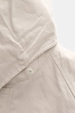 Nahaufnahme der Kapuze der 04651/ A trip in a bag Wachsjacke 'Sailor' sand/braun aus gewachster Baumwolle mit Druckknopf, Slim Fit, Cordbesatz, Windblende, Raglanärmel und geschmeidigem Flanellfutter, fotografiert aus seitlicher Perspektive.