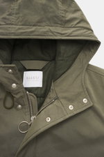 Nahaufnahme aus frontaler Perspektive des 04651/ A trip in a bag Parka 'Winter' oliv mit Kapuze, Baumwoll-Microfaser-Mix, weichem Griff, robustem Reißverschluss, Windblende mit Druckknöpfen, tonalem Futter.