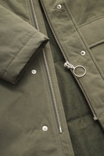 Nahaufnahme des olivfarbenen 04651/ A trip in a bag Parka 'Winter' mit robustem Reißverschluss, Druckknöpfen, weichem Griff, Oversized Fit, Kapuze und tonalem Futter.