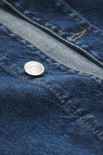Nahaufnahme der Fronttasche und der silbernen Sechs-Knopf-Leiste der dunkelblauen Brunello Cucinelli Jeansjacke aus reiner Baumwolle, Slim Fit mit Velourslederbesatz am Umlegekragen, fotografiert aus seitlicher Perspektive.