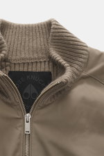 Close-up front view of the Moose Knuckles Down blouson 'Magnus Knit Hybrid' taupe featuring high-quality microfiber, knitted wool sleeves, soft touch, slim fit, durable two-way zipper, high ribbed collar, metal logo on upper arm, hip pockets with flap, li