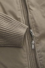 Close-up front view of Moose Knuckles Down blouson 'Magnus Knit Hybrid' taupe showing high-quality microfiber body, knitted wool sleeves, soft touch, durable two-way zipper, ribbed hem, and high closing ribbed collar.