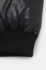 Close-up side view of black Moose Knuckles Down blouson 'King's Puffer' showing elastic hem and sleeve cuffs, high-quality microfiber, slim fit, warm down filling, two-way zipper, typical blouson collar made of ribbed knit, front pockets with snap button,
