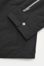 Close-up view of the Moose Knuckles Jacket 'Jacques' black sleeve, showing high-quality microfiber with a smooth feel, slim fit, robust two-way zipper, turn-down collar, patch chest pockets with flap, slanted welt pockets, metal logo on upper arm, cuff sl