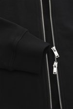 Close-up front view of the Moose Knuckles Sweat jacket 'Hartsfield Zip-Up' black, showing slim fit, pure cotton fabric, soft feel, robust two-way zip, ribbed cuffs, and signature metal emblem patch on sleeve. Features lined hood, integrated hip pockets, a