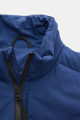 Nahaufnahme der Canada Goose Daunenweste 'Lodge' blau von schräg oben mit Ripstop-Obermaterial, wind- und wasserabweisend, Slim Fit, Stehkragen, Zwei-Wege-Reißverschluss und tonalen Details.