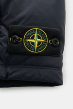 Close-up side view of Stone Island Daunenweste 'Seamless Tunnel Nylon Down' navy showing the embroidered black patch with yellow and green compass logo and button details on wind- and water-repellent high-quality microfiber fabric.