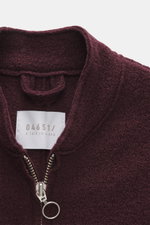 Nahaufnahme aus schräger Perspektive der bordeauxfarbenen 04651/ A trip in a bag Woll-Weste 'Boiled' mit Bouclé-Strick aus reiner Schurwolle, gewalkter Qualität, weichem Griff, Raw-Edge-Finish, Slim Fit, Metall-Reißverschluss, Stehkragen, aufgesetzter Bru