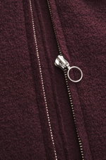 Nahaufnahme der Metall-Reißverschluss-Ziehgriffes der 04651/ A trip in a bag Woll-Weste 'Boiled' bordeaux aus Bouclé-Strick, gewalkte Qualität, weicher Griff, Raw-Edge-Finish, Slim Fit, Stehkragen, aufgesetzte Brusttasche, kleinem Weblabel in der Seitenna