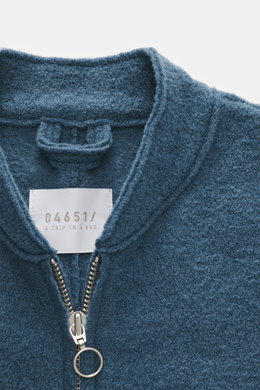 Nahaufnahme aus schräger Draufsicht der 04651/ A trip in a bag Woll-Weste 'Boiled' graublau mit Bouclé-Strick, Metall-Reißverschluss und Stehkragen, weicher Griff, Slim Fit, Raw-Edge-Finish, aufgesetzter Brusttasche, kleinem Weblabel, gewalkter Qualität, 