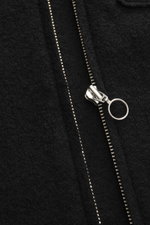 Schwarzer Metall-Reißverschluss in Nahaufnahme, Detailfoto der 04651/ A trip in a bag Woll-Weste 'Boiled' schwarz mit Bouclé-Strick, gewalkter Qualität, weichem Griff, Raw-Edge-Finish, Slim Fit, Stehkragen, aufgesetzter Brusttasche, kleinem Weblabel in de