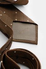 Close-up view of the folded Tom Ford Silk tie light brown/black/cream patterned, showing subtle sheen, herringbone with polka dots, and logo stitching.

Description: <p>Confident elegance down to the finest detail: This fine silk tie by TOM FORD is a styl