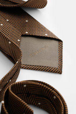 Close-up view of the folded Tom Ford Silk tie light brown/black/cream patterned, showing subtle sheen, herringbone with polka dots, and logo stitching.

Description: <p>Confident elegance down to the finest detail: This fine silk tie by TOM FORD is a styl