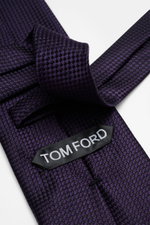 Tom Ford Seidenkrawatte dunkelviolett/schwarz gemustert, Nahaufnahme schräg von oben, reine Seide, dezenter Glanz, Hahnentrittmuster, Logo-Stitching, 8 cm breit, made in Italy.