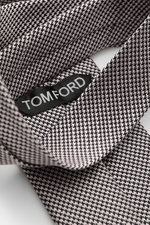 Nahaufnahme der Tom Ford Seidenkrawatte rosé/schwarz gemustert mit zeitlosem Hahnentrittmuster, dezentem Glanz und Logo-Stitching, fotografiert aus schräger Perspektive.