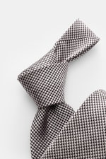 Tom Ford Seidenkrawatte rosé/schwarz gemustert mit zeitlosem Hahnentritt, Logo-Stitching, reine Seide, dezenter Glanz, Detail von oben fotografiert.