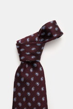 Nahaufnahme der Zegna Seidenkrawatte bordeaux/rauchblau gemustert mit Paisley Webmuster, dezentem Glanz, ca. 8 cm breit, reine Seide, kontrastfarbener Futterstoff, Made in Italy, fotografiert von schräg oben.