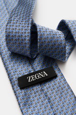Nahaufnahme der Zegna Seidenkrawatte hellblau/hellgrau/schwarz gemustert mit grafischem Muster, dezenter Glanz, reine Seide, Made in Italy, Breite ca. 8 cm, schräg fotografiert.