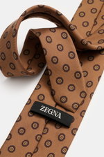 Nahaufnahme der Zegna Seidenkrawatte hellbraun/dunkelbraun gemustert mit floralem Webmuster, dezentem Glanz, Futterstoff kontrastfarben, reine Seide, Made in Italy, ca. 8 cm breit, aus schräger Perspektive fotografiert.