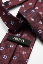 Nahaufnahme aus schräger Perspektive einer Zegna Seidenkrawatte schwarz/bordeaux/hellgrau gemustert mit feinem Webmuster, dezentem Glanz, monochromem Futterstoff, reine Seide, Made in Italy, Breite ca. 8 cm.
